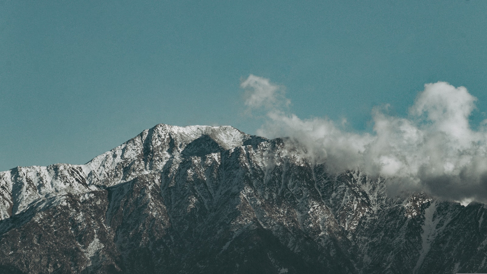 a snow covered mountain range with clouds in the sky